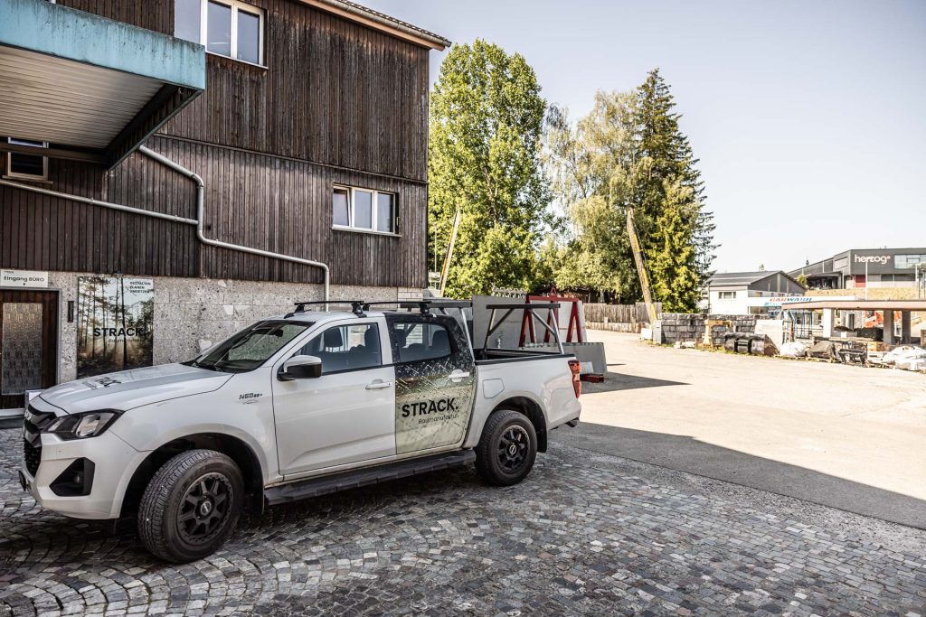 Beschrifteter Pick-up der STRACK Baumanufaktur vor der Holzfassade