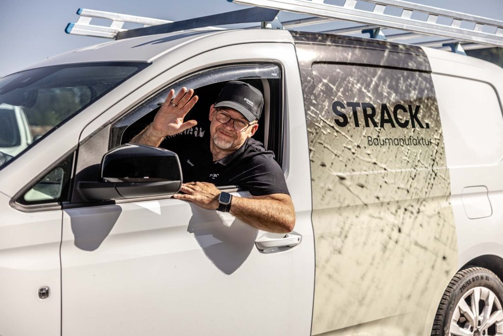 Fahrer winkt aus dem beschrifteten Lieferwagen der STRACK Baumanufaktur