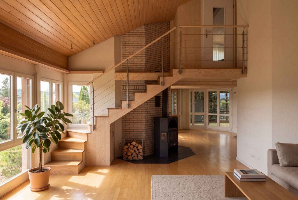 Wohnraum mit Massivholztreppe zur Galerie und Backsteinkamin bei Tageslicht