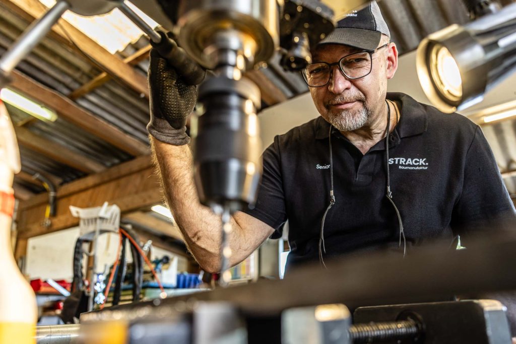 Metallbauer der STRACK Baumanufaktur bohrt konzentriert ein Stahlteil