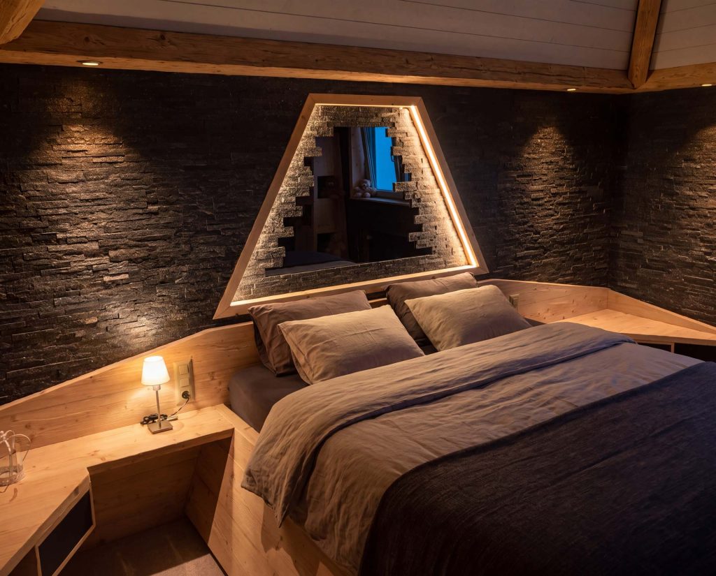 Schlafzimmereinbau mit beleuchteter Nische vor einer Steinwand