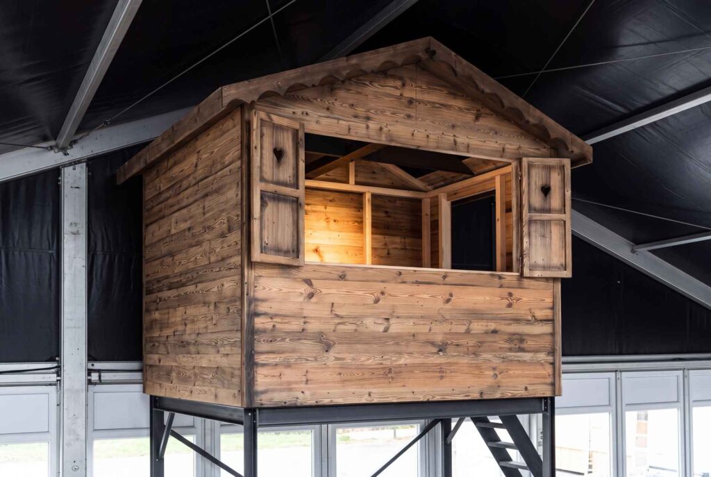 Hüttenkubus aus Altholz auf Stahlkonstruktion, eingebaut in eine Eventhalle