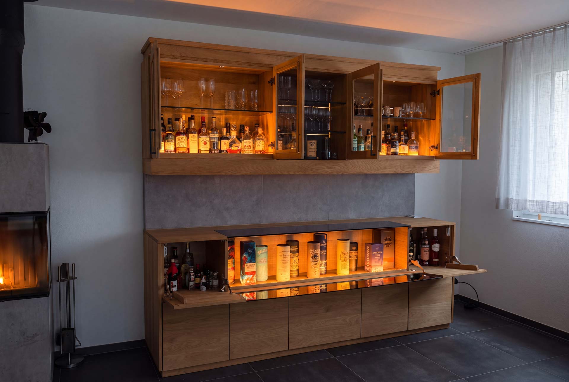 Fertige Whiskybar in Eiche: beleuchtetes Sideboard mit geöffneten Klappen und verglaste Hängeschränke für Gläser